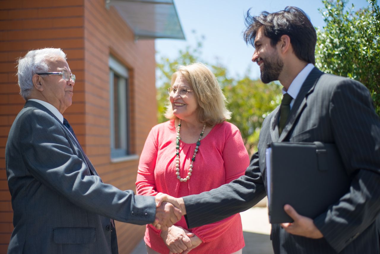 Menu Real estate agent and mature couple shaking hands outdoors, sealing a deal with smiles.