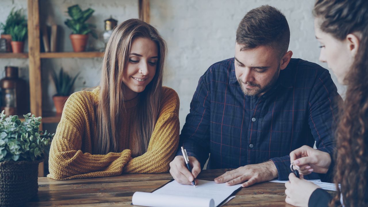 About Three adults in a casual office setting reviewing and signing documents.